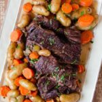 Pot Roast with vegetables and herbs on a white rectangular platter.