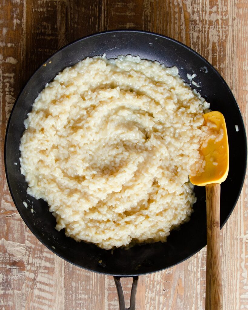 Risotto in a skillet with a yellow spatula.