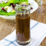 Simple Vinaigrette in a glass cruet with a salad behind.