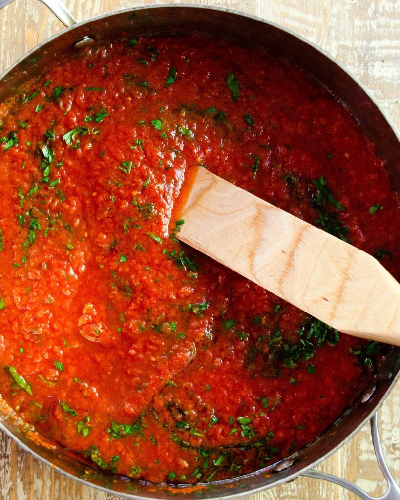 Marinara Sauce in a large saute pan with a wooden spoon.