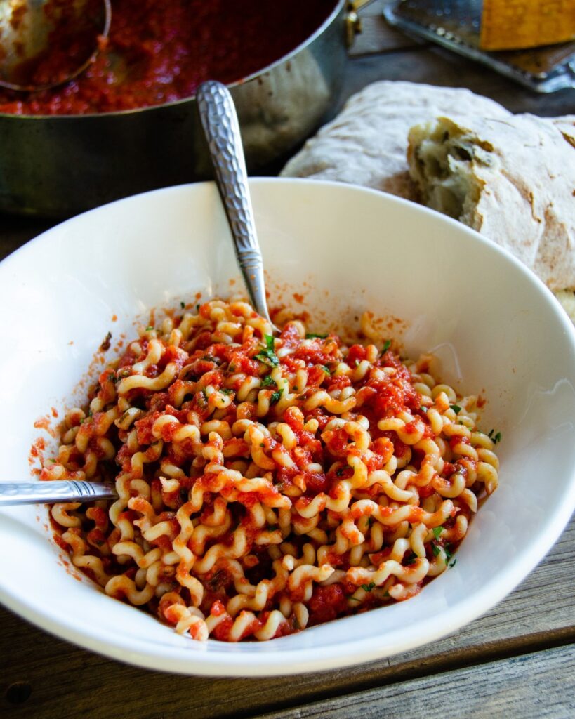 Long Fusilli with marinara sauce in a white bowl with spoon and fork.