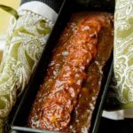 Meatloaf in a loaf pan with green oven mitts holding each side.