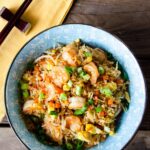 Shrimp Fried Rice in a blue bowl on a wooden table with a yellow napkin and chopsticks.