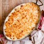 Potato gratin in a copper oval gratin pan on a wooden table.