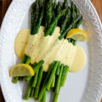 An oval platter of asparagus with hollandaise sauce poured over top.