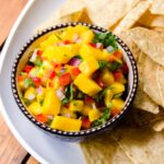 Mango Salsa in a blue bowl on a white platter with tortilla chips.