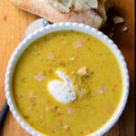 Split Pea Soup in a white bowl on a wooden table with ripped bread and a spoon.