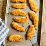 Chicken Fingers on a baking tray with spatula and towel.