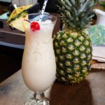 Pina Colada in a tulip glass next to a pineapple.