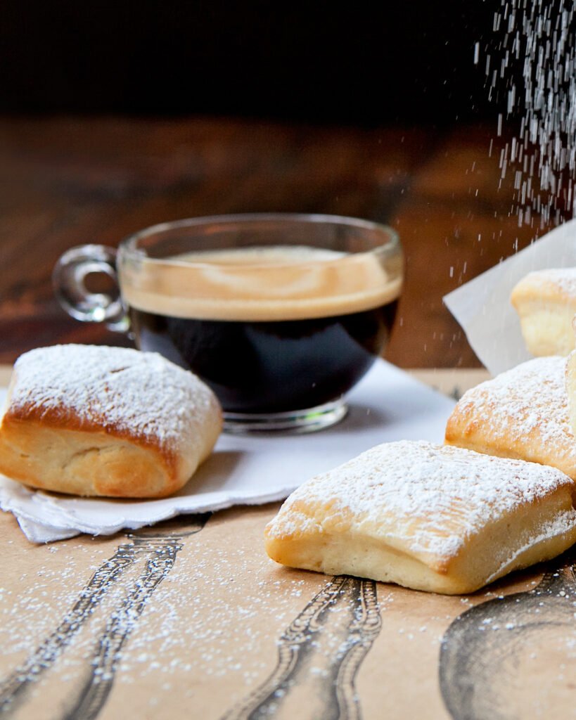 A couple of beignets in front of a cup of espresso.