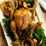 Roast chicken on a rectangular platter with delicata squash and kale.