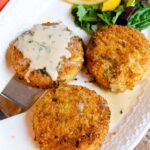 Crab cakes with sherry sauce on a white platter.