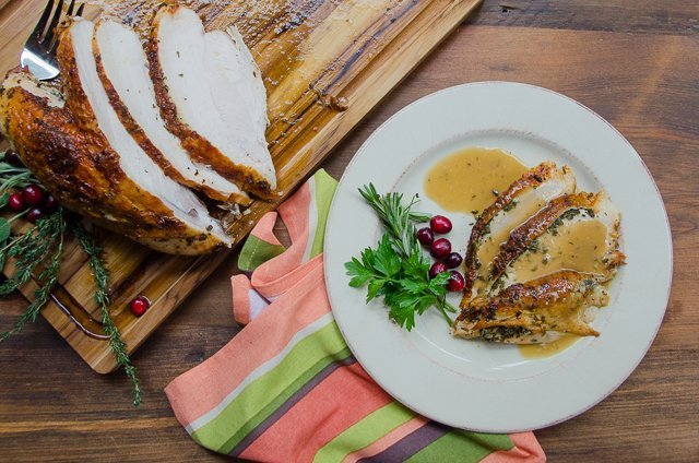 A white plate with slices of roast turkey breast covered with gravy in foreground; whole turkey breast on cutting board in background.