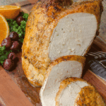 Air fried turkey breast on a wooden board with several slices already cut.