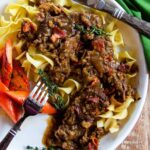 Beef Carbonnade with egg noodles on a white plate with knife, fork and green napkin.