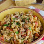 Beef and macaroni in a large yellow bowl with parmesan cheese and a grater near by.