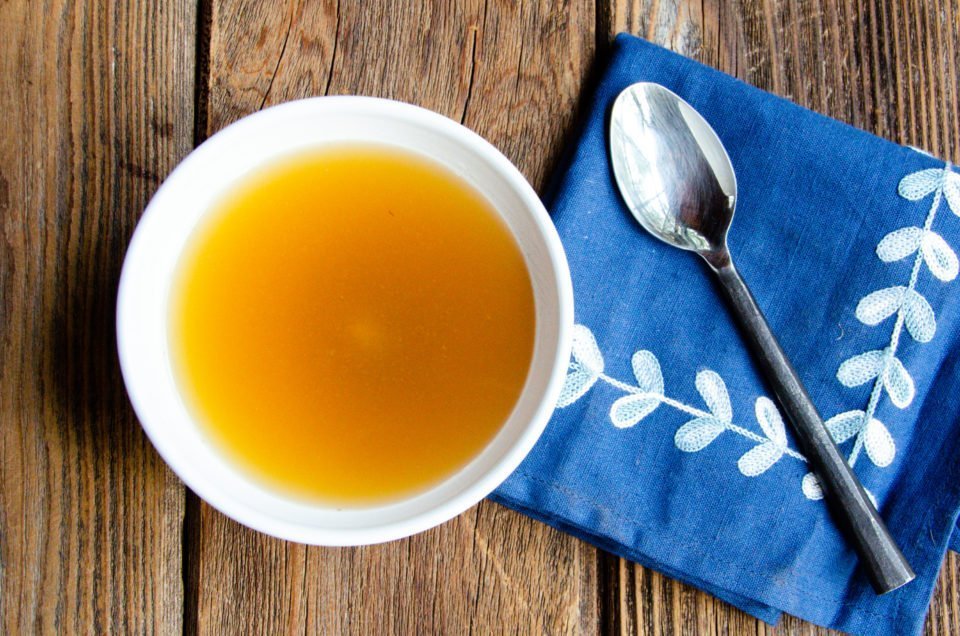 A white bowl of bone broth on a wooden table.