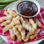 Air fried sugared dough dippers on a plate with chocolate sauce.