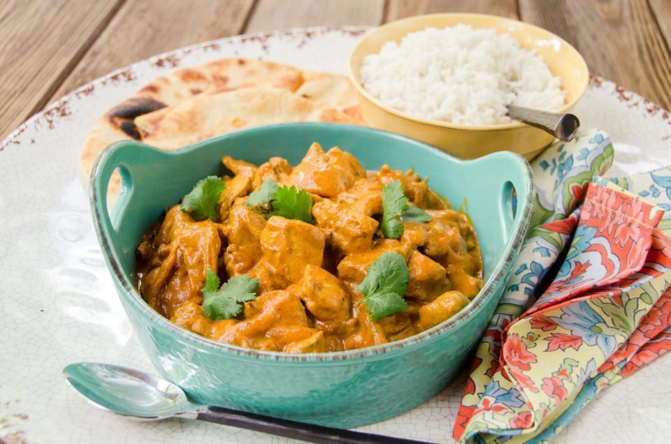 Butter chicken in a green casserole with white rice and naan in the background.