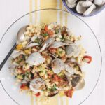 Cavatapi con Vongole in a glass bowl on a tablecloth with a yellow line with empty clam shells nearby.