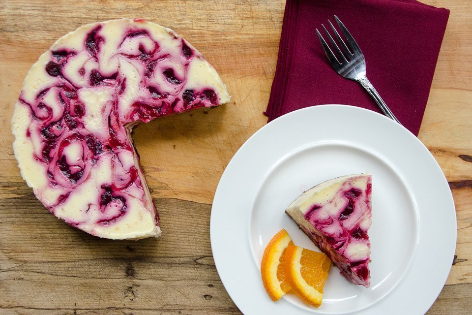 Orange Cranberry Cheesecake on a wooden board with a piece cut out on a white plate.