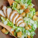 Chicken Caesar Salad in a wooden salad bowl with croutons and a sliced chicken breast.