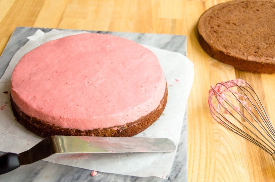 Chocolate cake being assembled with a layer of raspberry mousse on one layer.