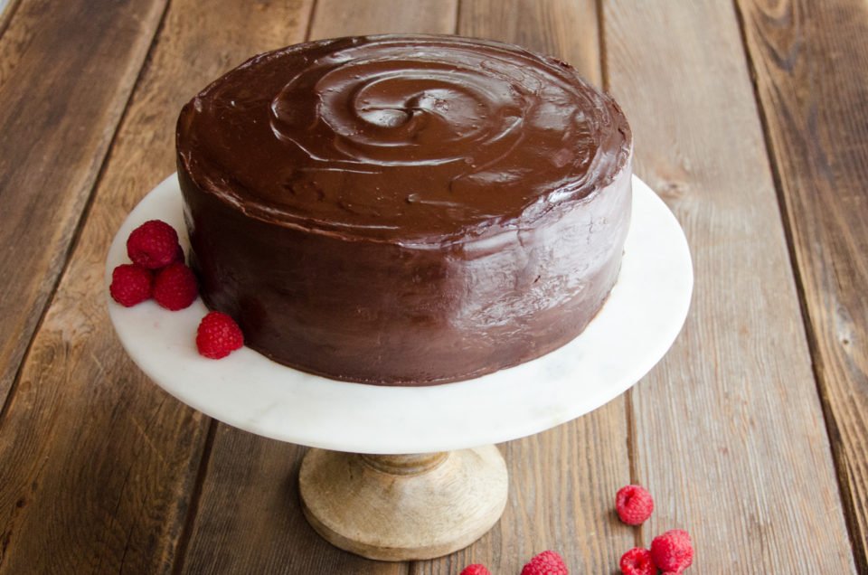 Whole Chocolate Cake on a cake stand with raspberry garnish.