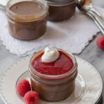 chocolate raspberry pots de creme in jars on a white plate with raspberries
