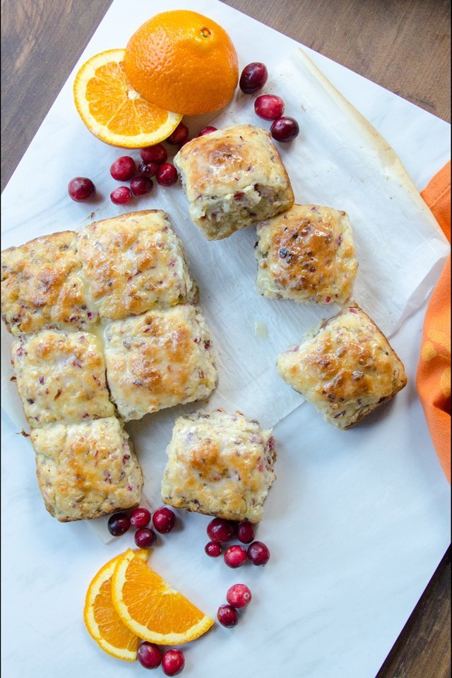 Cranberry Orange Pecan Buttermilk Biscuits on a piece of parchment paper with oranges and cranberries around.