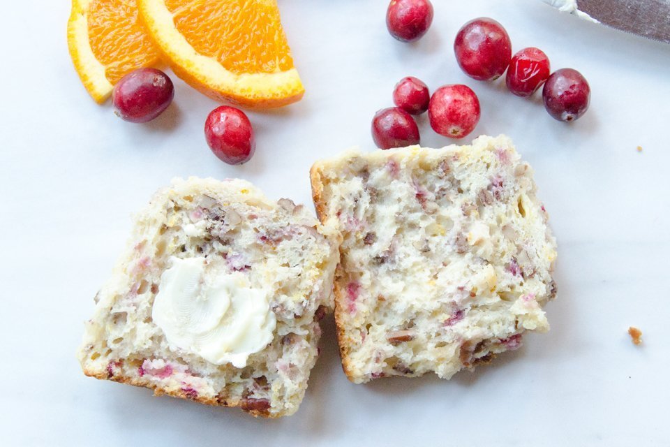 Close up of a cranberry orange pecan buttermilk biscuit with a few cranberries and an orange slice.