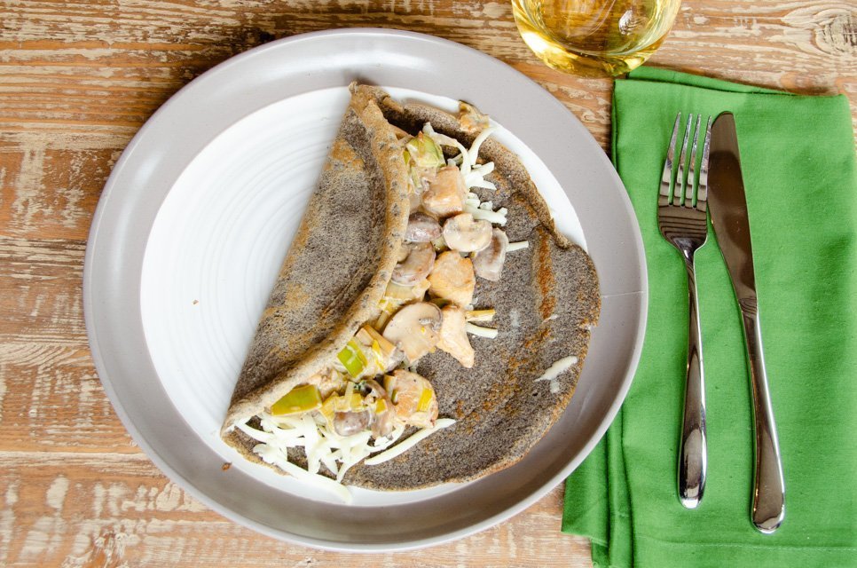 One buckwheat crepe with chicken on a plate, just before being rolled up.