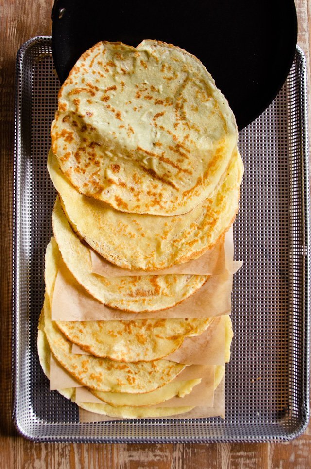Crêpes shingled on a perforated sheet pan and a skillet sliding the last one out.
