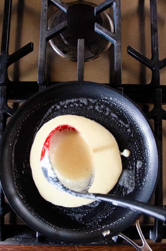 A ladle pouring batter into a crêpe pan.