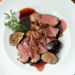 Duck breast with roasted figs and pomegranate molasses on a white plate on a wooden table.