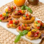 Tricolor tomato bruschetta on a serving platter on a rattan placemat.