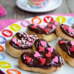 Chocolate Eclair Hearts decorated with pink and red hearts on a white plate with a cup of tea in the background.