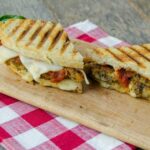 Eggplant Parmesan Panini on a wooden board with a red checkered napkin.