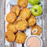 Fried Green Tomatoes on a white tray with raw green tomatoes on the side.