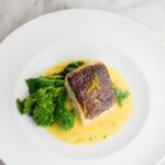 Halibut with orange butter on a white plate with broccoli rabe.