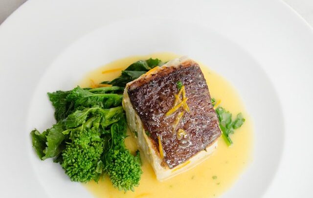 Halibut with orange butter on a white plate with broccoli rabe.