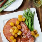Ham steak with pineapple and brown sugar glaze on a white plate with asparagus.