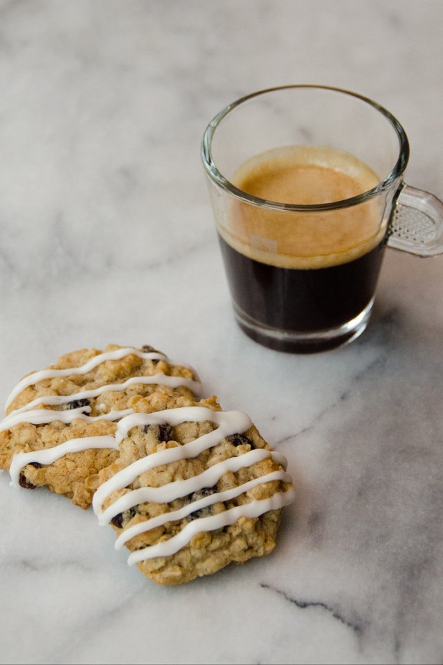 Two iced oatmeal raisin cookies on a marble counter with an espresso.