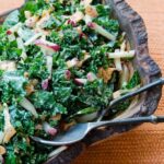 Kale and Carrot slaw in a rustic wooden bowl on an orange placemat.