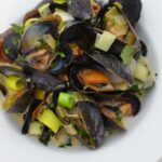 Mussels with beer, leeks and cream in a white bowl.