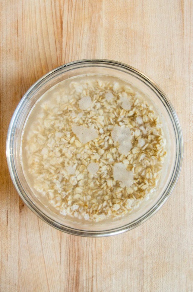 A glass bowl with oats soaking in preparation for homemade oat milk.