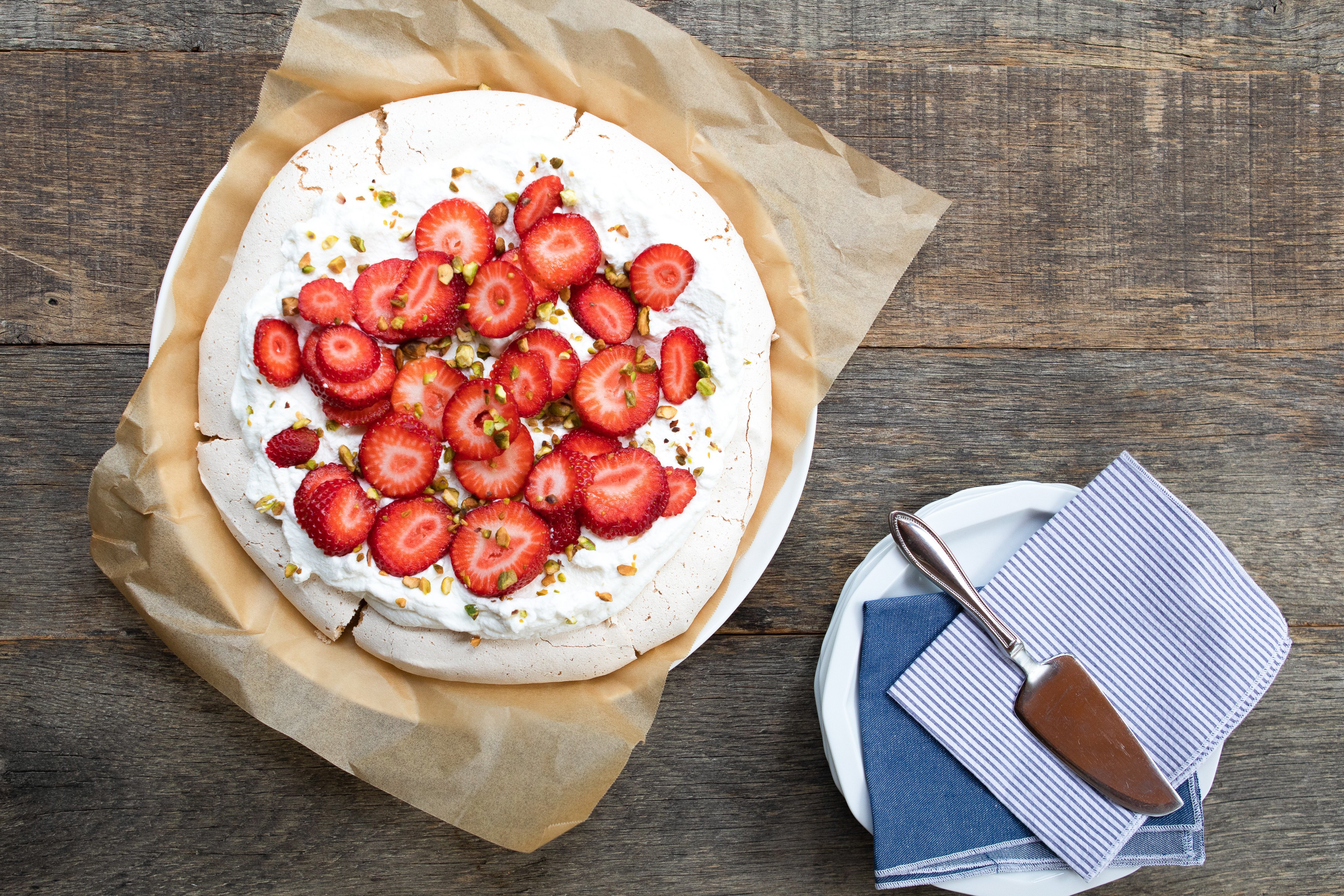 Whole Pistachio Pavlova with Strawberries with a stack of side plates and denim napkin.