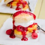 Peach Melba Shortcake on a white plate on a yellow wooden table.