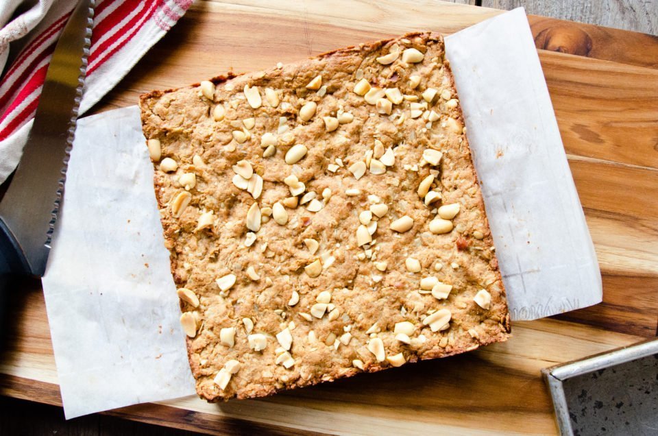 Peanut butter breakfast bars before they are cut on a wooden cutting board.