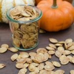Air-fried pumpkin seeds on a wooden table with gourds in the background.